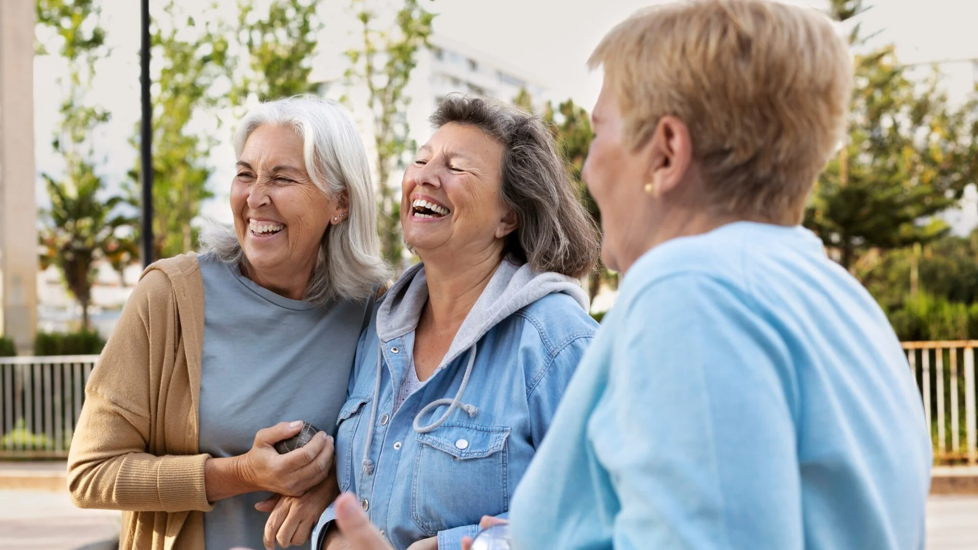 Three women smiling together in sunny weather.