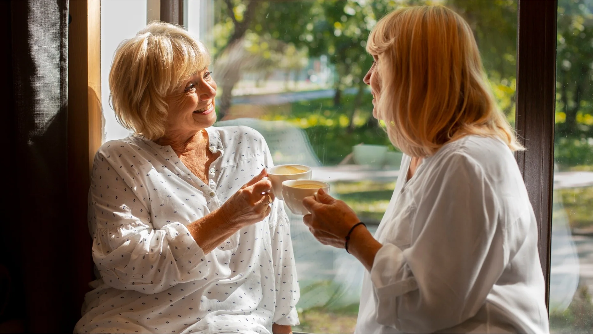Two women sharing tea at home near a window.