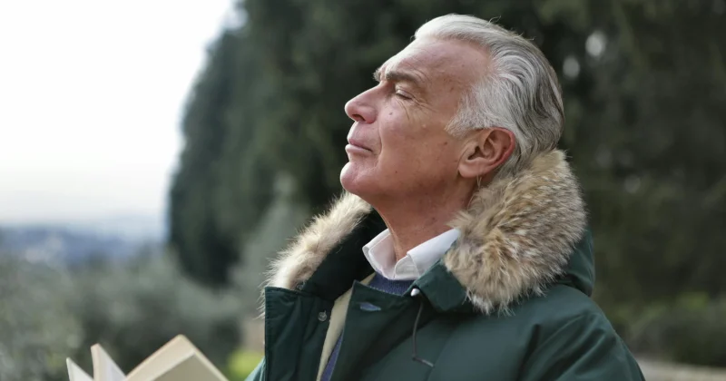 Elderly man in fur-lined coat outdoors.