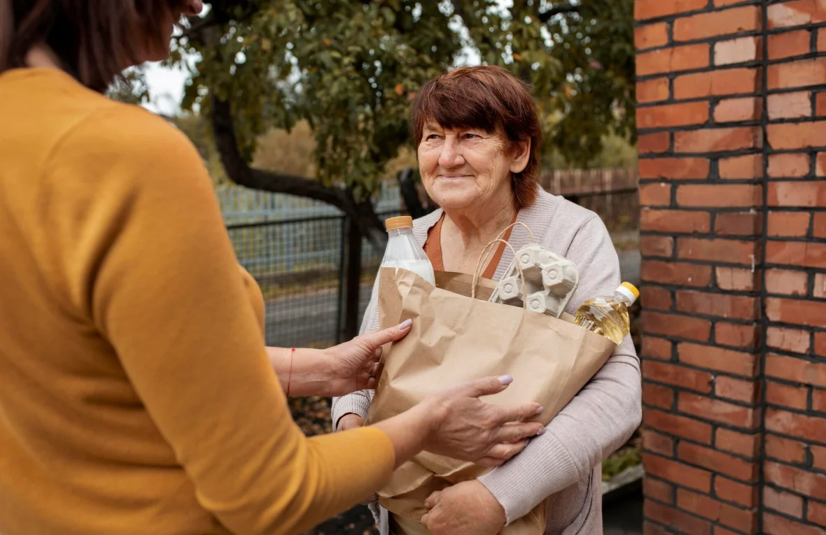 Young woman delivering groceries to another female outdoors.