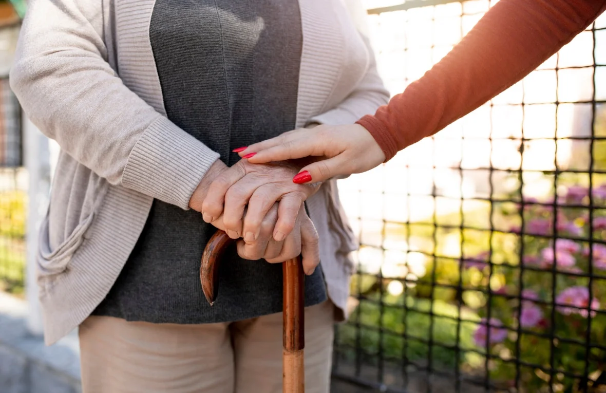 Young hand comforting elderly person's hand on cane.
