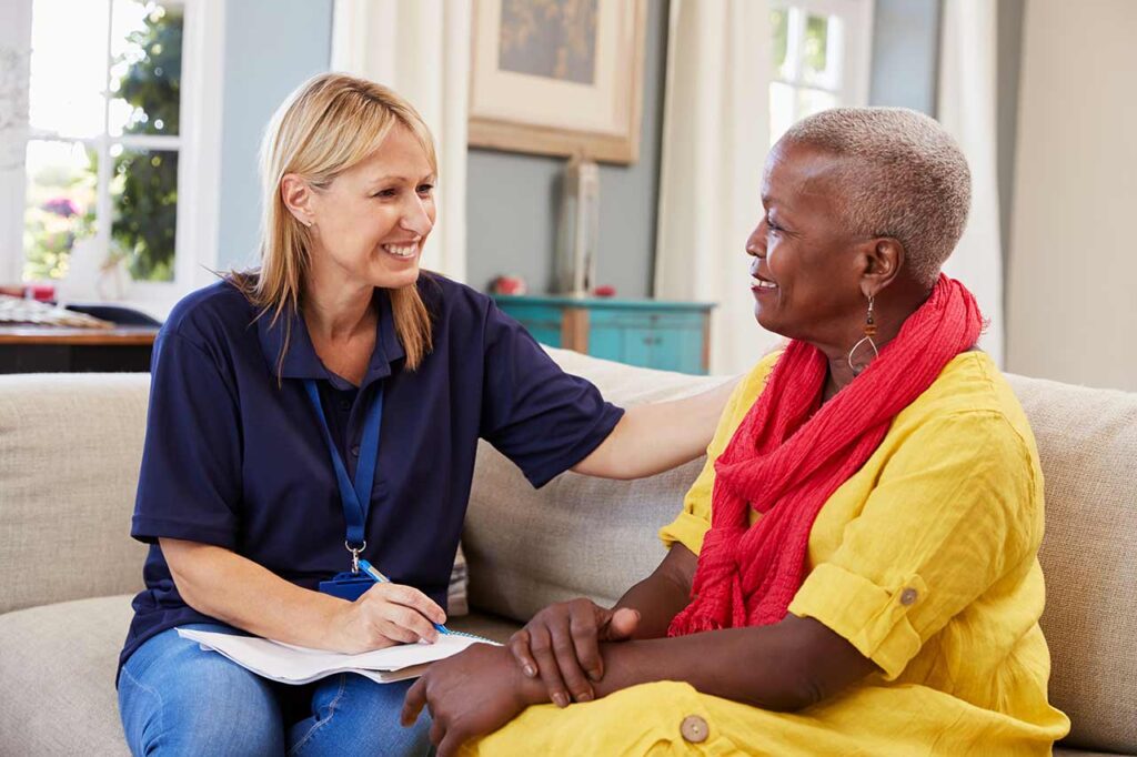 Caregiver talking with elderly woman in yellow shirt.
