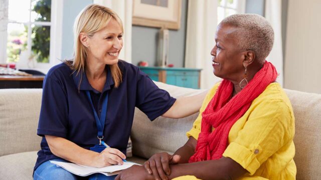 Caregiver talking with elderly woman in yellow shirt.