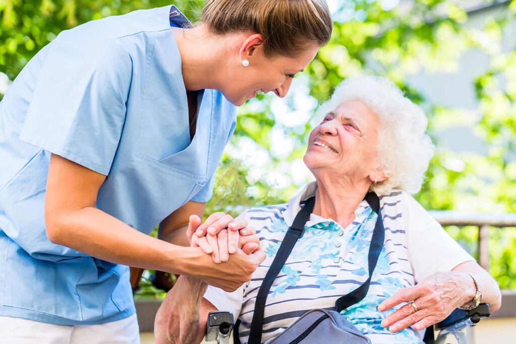 Nurse holding hands with elderly patient outside.