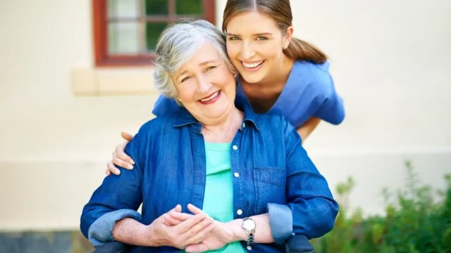 Young woman supporting senior in wheelchair outdoors.
