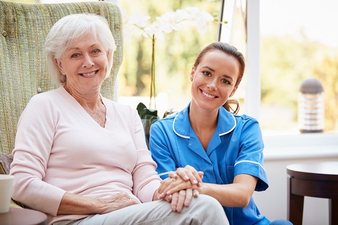 Caregiver and older woman holding hands on the sofa.