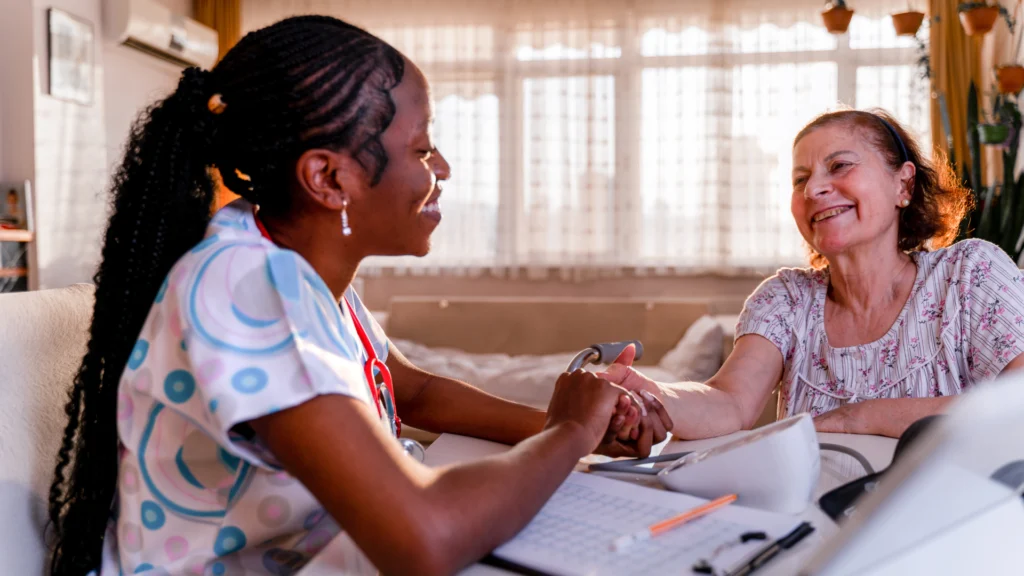 A caregiver and elderly woman sit at a table, looking through a notebook and sharing a conversation