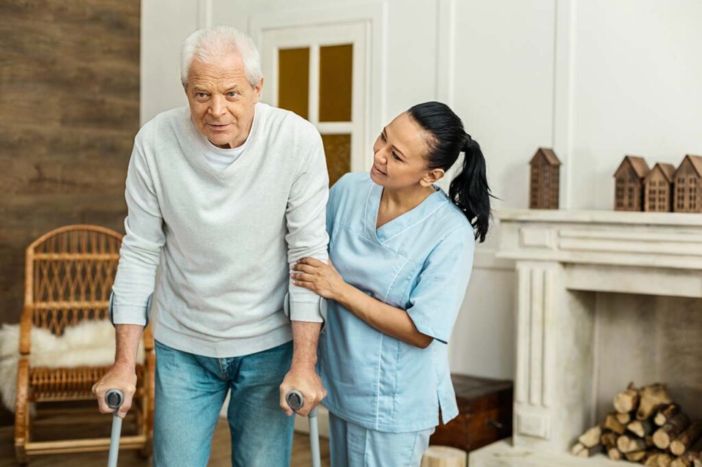 Nurse helping elderly man stand with walker at home.
