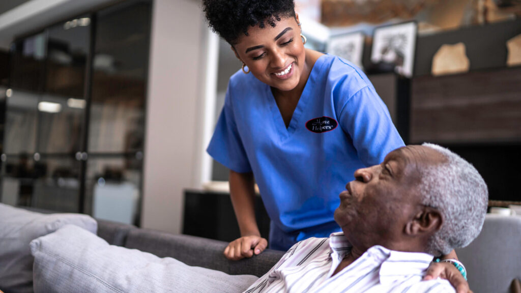 Young nurse explaining medication to older man on couch.
