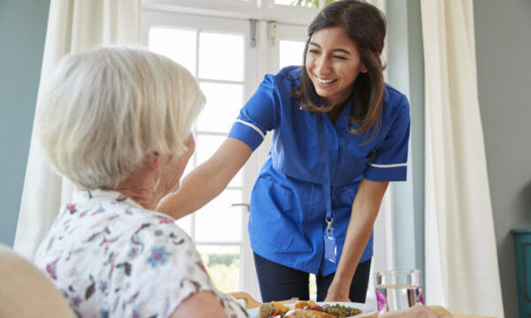 Care nurse serving dinner to a senior woman at home
