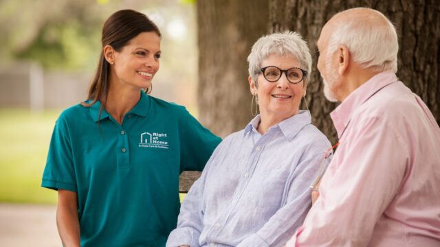 Caregiver assisting seniors seated outdoors.