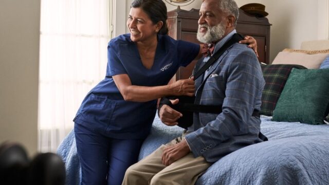 Physiotherapist guiding elderly man with arm stretch at home.