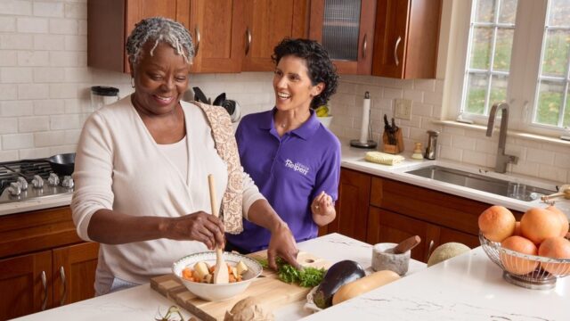 Senior and caregiver preparing vegetables together in kitchen.