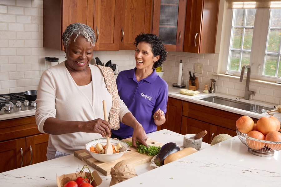 Senior and caregiver preparing vegetables together in kitchen.