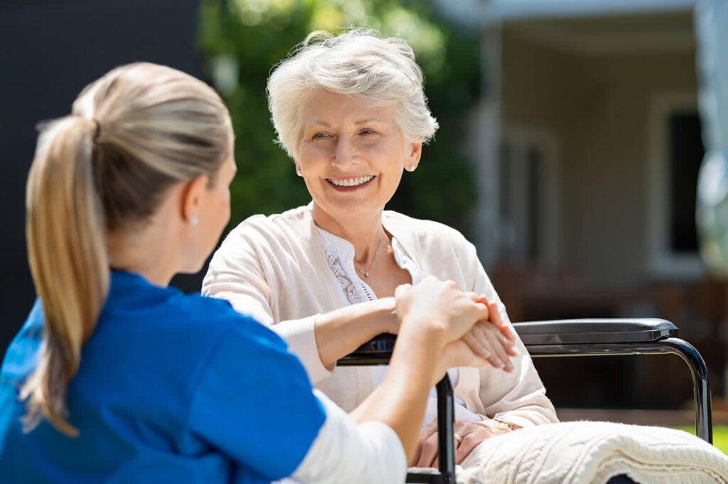 A doctor in blue scrubs attends to an elderly woman sitting in a wheelchair, ensuring her comfort.