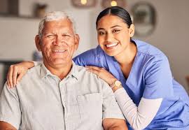 A caregiver in blue scrubs smiles with an elderly man, both enjoying a joyful moment together.