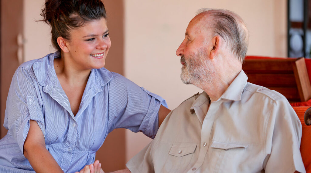 A caregiver and an old man having a thoughtful conversation in a cozy room, both smiling.