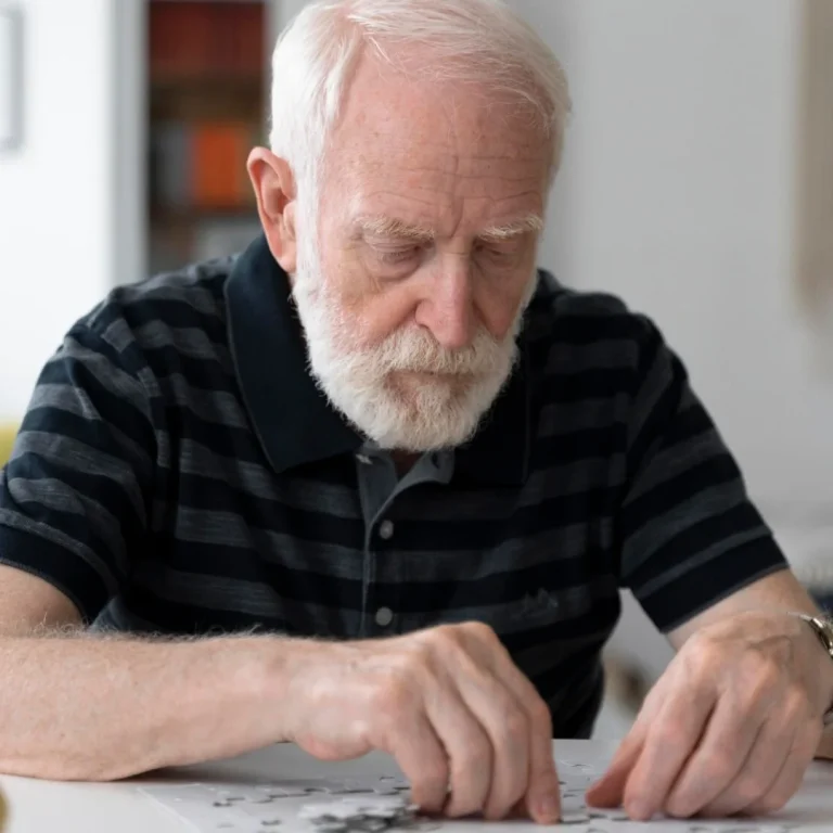 Elderly man working on a puzzle at a table.